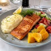 Plated dish of salmon with mashed potatoes and vegetables on a table setting.
